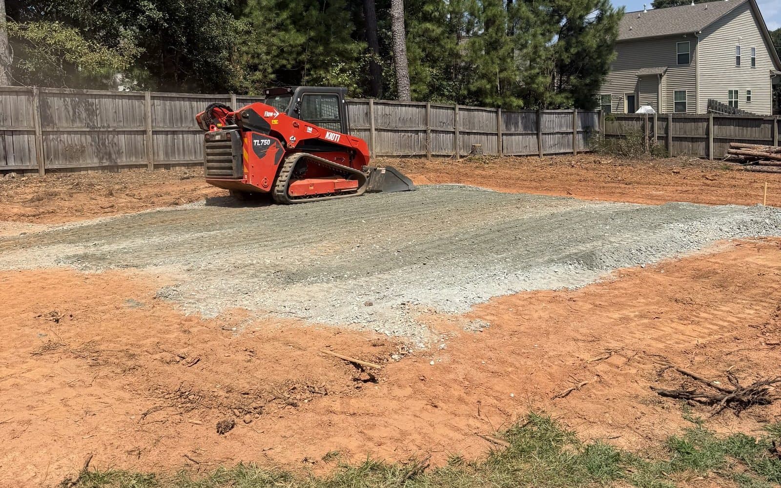 Kioti TL750 grading a crusher-run gravel pad in a fenced backyard in Upstate SC